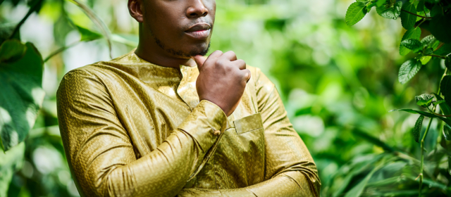 Ein nachdenklicher Herr, gekleidet in einem eleganten, goldenen Gewand mit feiner Musterung von Getzner Textil.