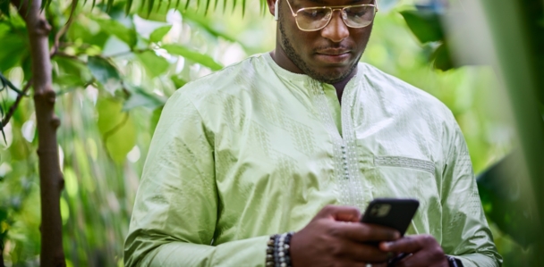Mann in hellgrünen Boubou schaut auf sein Handy